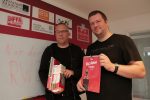 Karsten Plewnia und Tami Capitain vor der Sponsorenwand der Essener Chancen mit dem FFA Kalender 2018 und den von den Spenden gekauften neuen Schulbüchern